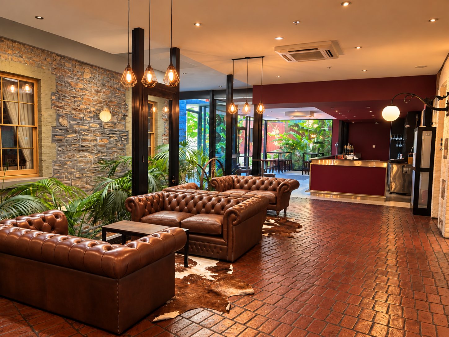 Henry’s Bar, leather Chesterfield sofas on terracotta tiles with the bar and a planted courtyard beyond