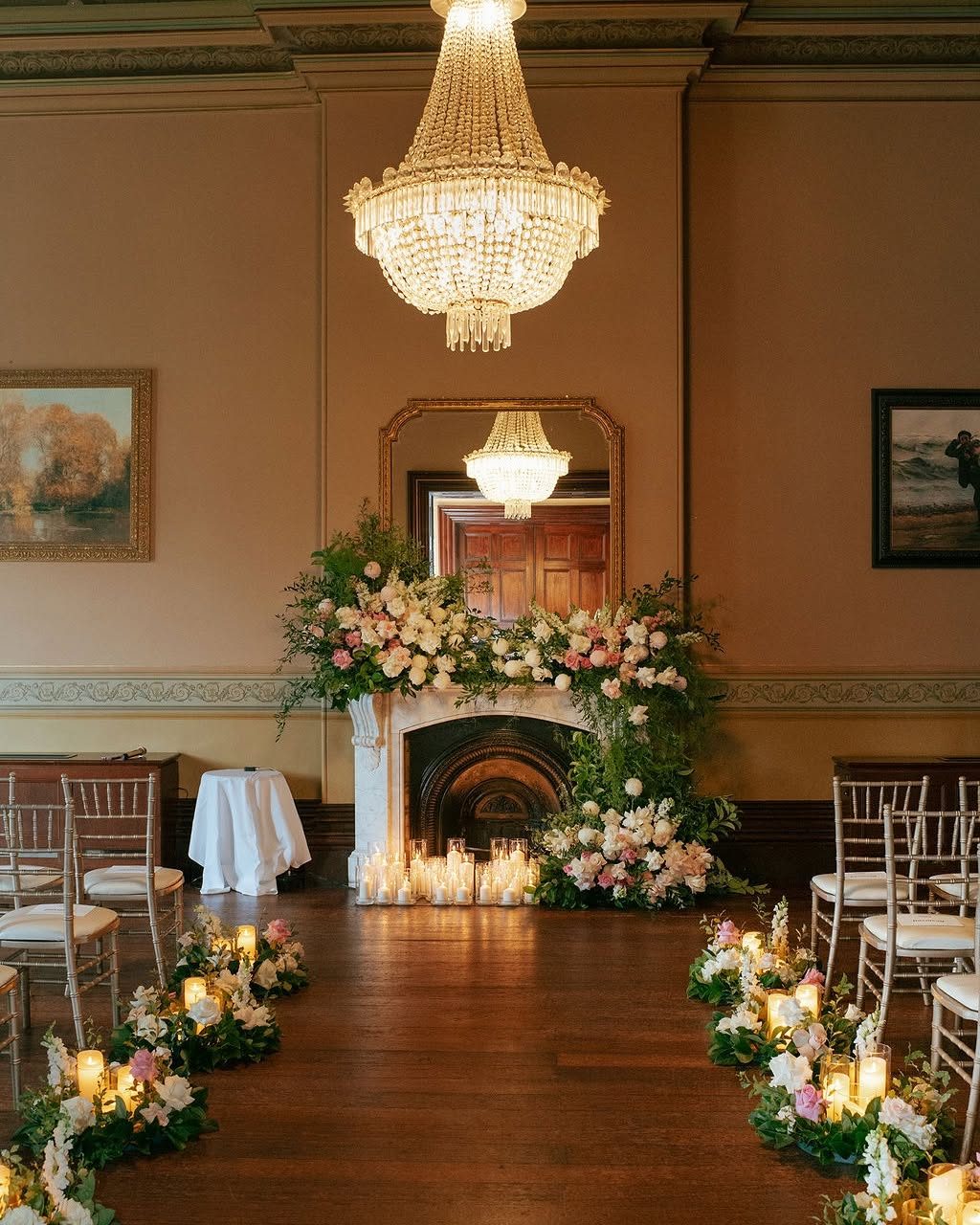 The Ballroom set for a ceremony, flowers and candles at the marble fireplace beneath the chandelier