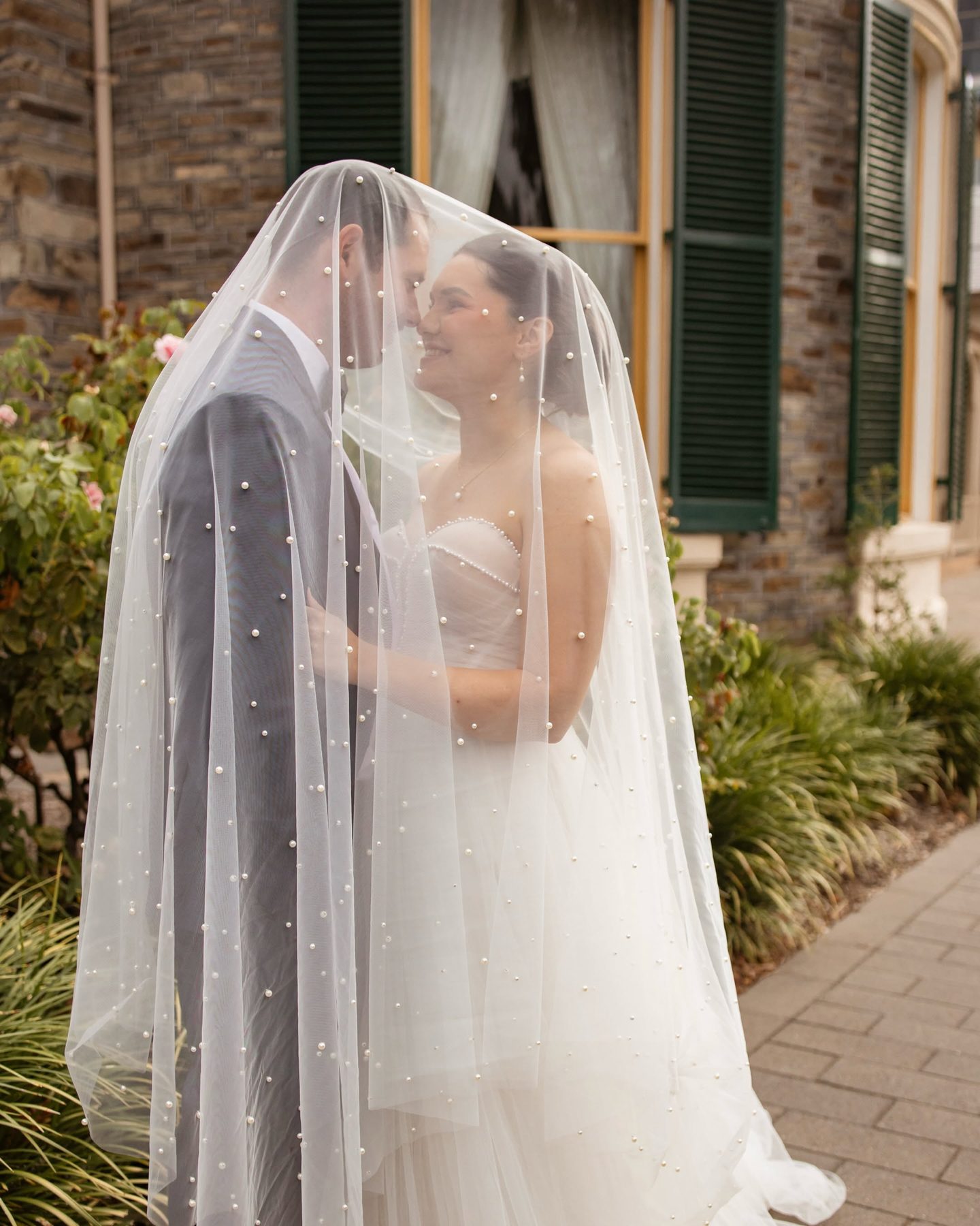 A couple under a pearl veil outside the bluestone wall and green shutters of Ayers House